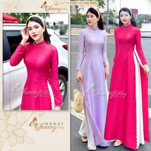 May include: Two women wearing long, traditional Vietnamese dresses called áo dài. One dress is a vibrant pink with white trim, and the other is a soft lavender with white trim. Both dresses feature pearl accents and side slits.