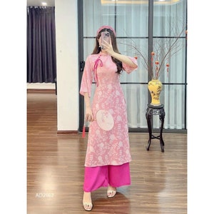 May include: A pink and white floral print dress with a pink sash and matching pink pants. The dress has a mandarin collar and three-quarter sleeves. The model is holding a white fan with a pink tassel.