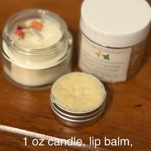 Puede incluir: Kit #2 incluye una vela de 30 ml, bálsamo labial y exfoliante de sal. La vela está en un frasco de vidrio transparente con tapa blanca y flores secas en la parte superior. El bálsamo labial está en una lata de plata. El exfoliante de sal está en un frasco blanco con tapa blanca.