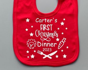 May include: Red baby bib with white text that says "Carter's First Christmas Dinner 2023" with a turkey, carrot, fork, and knife graphic.