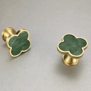May include: Two brass cabinet knobs with a green clover-shaped design. The knobs have a smooth, polished finish.