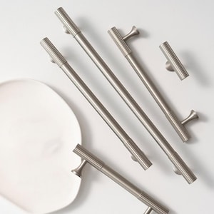 May include: Five silver cabinet pulls with a fluted design. The pulls are in various sizes and styles, including a long bar pull, a short bar pull, and a knob pull.