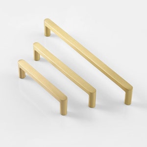 Könnte beinhalten: Drei gebürstete goldene Schrankgriffe in verschiedenen Längen. Die Griffe sind rechteckig mit abgerundeten Kanten.