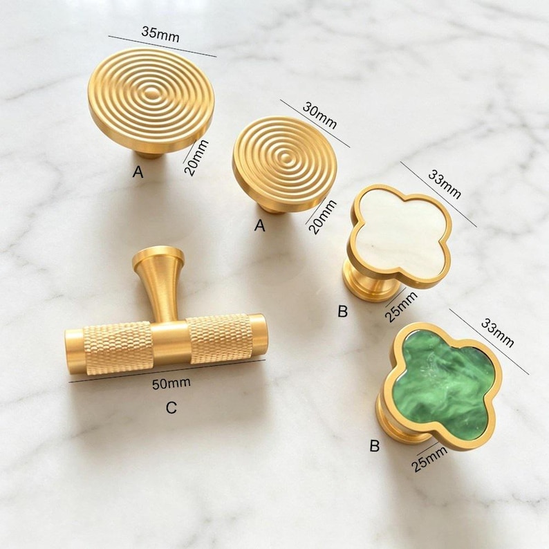 Peut inclure: Une collection de boutons et poign&eacute;es de placard dor&eacute;s. Deux boutons ronds &agrave; cercles concentriques mesurent 35mm et 30mm de diam&egrave;tre. Deux boutons en forme de tr&egrave;fle avec incrustations blanches et vertes mesurent 33mm. Une poign&eacute;e en T molet&eacute;e mesure 50mm.