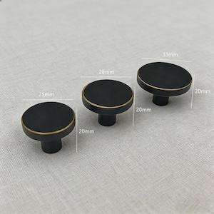 Puede incluir: Tres pomos de armario negros con bordes dorados. Los pomos tienen un dise&ntilde;o redondo y miden 25 mm, 28 mm y 33 mm de di&aacute;metro. Cada pomo mide 20 mm de alto.