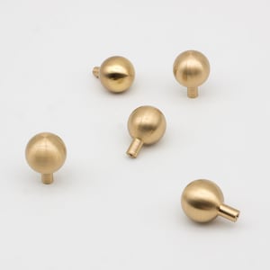 May include: Five gold-toned round cabinet knobs with a smooth, polished finish. Each knob has a small, round base.