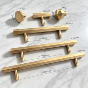 May include: A collection of brushed gold cabinet hardware including three hexagonal and T-shaped knobs and three long bar pulls. The hardware features labelled dimensions: knobs at 21mm by 34mm, 50mm by 28mm, and 35mm, with bar pulls at 150mm, 180mm, and 220mm lengths.