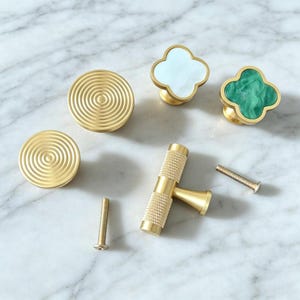 Peut inclure: Un ensemble de quincaillerie d'ameublement comprenant deux boutons ronds en laiton avec des motifs de cercles concentriques, un bouton en forme de tr&egrave;fle avec incrustation blanche, un bouton en forme de tr&egrave;fle avec incrustation verte et deux vis.