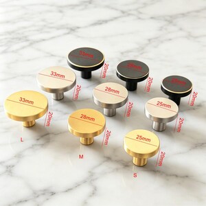 May include: A collection of nine round cabinet knobs in gold, silver, and black finishes. The knobs are arranged in three sizes labelled L, M, and S, with diameters of 33mm, 28mm, and 25mm respectively, and a consistent height of 20mm as marked.