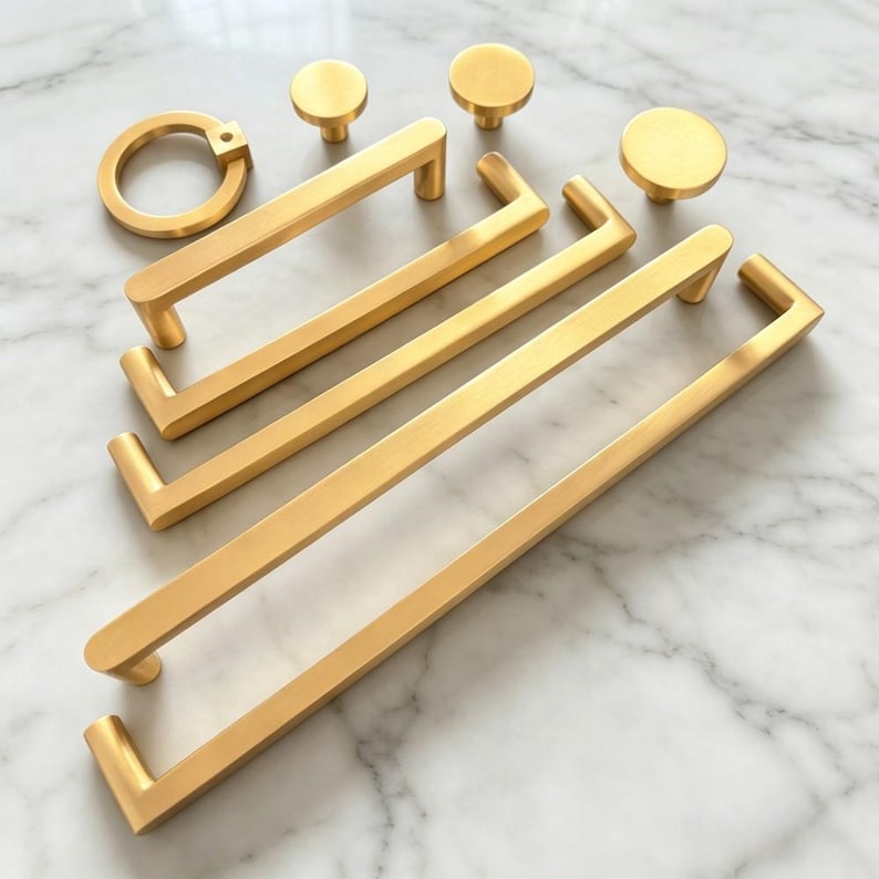 Peut inclure: Une collection de quincaillerie en or bross&eacute; comprenant trois poign&eacute;es de placard rectangulaires de longueurs vari&eacute;es, une poign&eacute;e annulaire circulaire et trois boutons de placard ronds. Chaque pi&egrave;ce pr&eacute;sente une finition m&eacute;tallique mate.