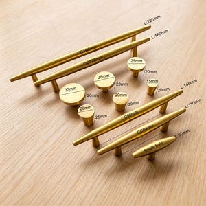 May include: A collection of brushed gold cabinet hardware including various sizes of bar pulls and round knobs. The pulls feature centre-to-centre measurements of 64mm, 96mm, 128mm, and 160mm, while the knobs range from 15mm to 33mm in diameter.