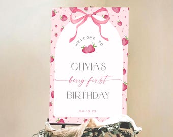 May include: A pink and white welcome sign with a pink bow and strawberry pattern. The sign reads "Welcome to Olivia's Berry First Birthday 04.13.25".