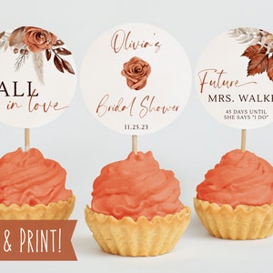 May include: Three cupcake toppers with autumn-themed designs. The toppers feature a floral design with autumnal colours, the text "FALL in love", "Olivia's Bridal Shower 11.25.23", and "Future MRS. WALKER 45 DAYS UNTIL SHE SAYS "I DO"".