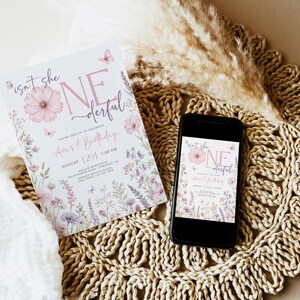 May include: A rectangular birthday invitation card and a smartphone displaying the same invitation design. The design features pink flowers, butterflies, and the text "isn't she ONEderful" with event details for Ava's 1st Birthday on August 29th.
