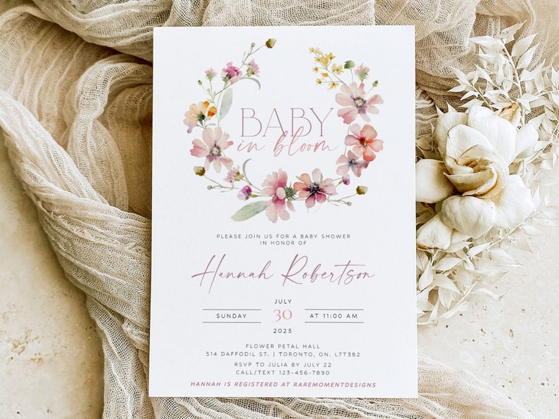 Peut inclure: Une invitation &agrave; une f&ecirc;te pr&eacute;natale avec une couronne florale aquarelle et le texte "BABY in bloom". L'invitation est pour Hannah Robertson et est pr&eacute;vue pour le dimanche 30 juillet &agrave; 11h00. L'&eacute;v&eacute;nement aura lieu au Flower Petal Hall, 514 Daffodil St., Toronto, ON. L7T582. RSVP &agrave; Julia avant le 22 juillet. Appelez/textez au 123-456-7890. Hannah est inscrite chez Raremomentdesigns.