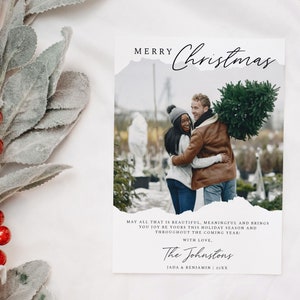 May include: A Christmas card with a photo of a couple holding a Christmas tree. The card has a white background with black text that reads "Merry Christmas" and "May all that is beautiful, meaningful and brings you joy be yours this holiday season and throughout the coming year: With love, The Johnstons JADA & BENJAMIN 20XX".
