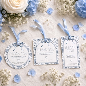 Puede incluir: Tres etiquetas de regalo de papel en formas redonda, cuadrada y rectangular, cada una con un patrón floral azul, una cinta azul y el texto THANK YOU FOR SHOWERING MAISIE WITH SO MUCH LOVE! MAISIE'S BRIDAL SHOWER AUGUST 24, 2026 con un icono de corazón.