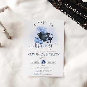K&ouml;nnte beinhalten: Eine Babyparty-Einladung mit einem blauen und wei&szlig;en Aquarell-Design. Die Einladung zeigt einen Kessel mit einer schwarzen Katze und K&uuml;rbissen. Der Text lautet "Ein Baby braut sich zusammen" und "Veronica Hudson".