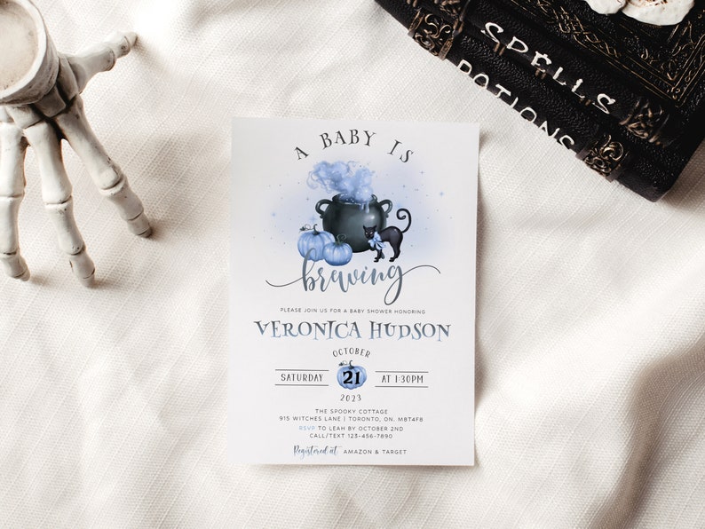 K&ouml;nnte beinhalten: Eine Babyparty-Einladung mit einem blauen und wei&szlig;en Aquarell-Design. Die Einladung zeigt einen Kessel mit einer schwarzen Katze und K&uuml;rbissen. Der Text lautet "Ein Baby braut sich zusammen" und "Veronica Hudson".