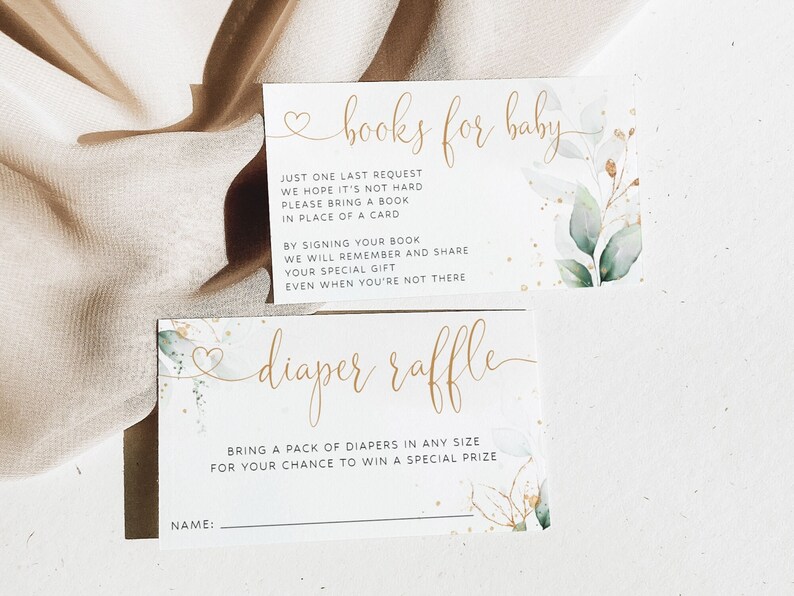 May include: Two white cards with gold lettering and watercolor greenery. The top card says "books for baby" and has instructions for guests to bring a book instead of a card. The bottom card says "diaper raffle" and has instructions for guests to bring a pack of diapers for a chance to win a prize.