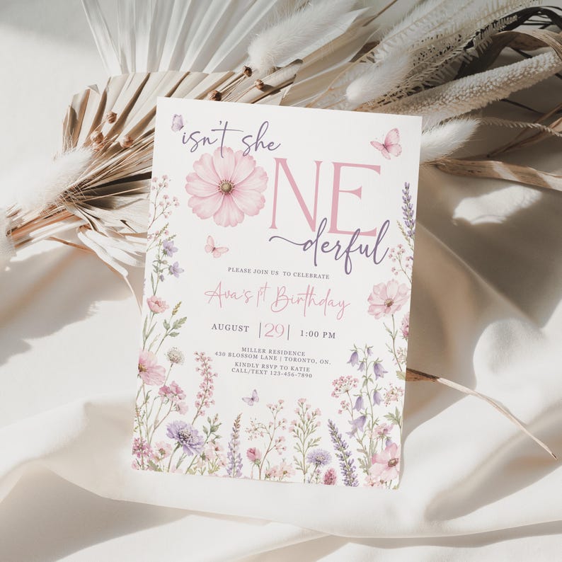 May include: A rectangular birthday invitation card featuring a white background with pink and purple floral illustrations, butterflies, and the text "isn't she ONEderful" in pink and dark purple script and serif fonts, detailing event information.