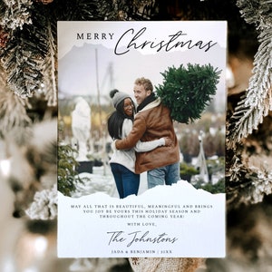 May include: A Christmas card with a photo of a couple holding a Christmas tree. The card has a white background with a blue and white watercolor design. The text on the card reads "Merry Christmas" and "May all that is beautiful, meaningful and brings you joy be yours this holiday season and throughout the coming year! With love, The Johnstons Jada & Benjamin 20XX".