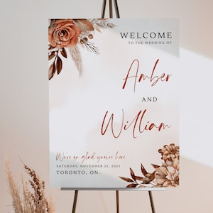 May include: A wedding welcome sign featuring a floral design in shades of brown and orange. The sign reads "Welcome to the wedding of Amber and William. We're so glad you're here. Saturday, November 25, 2023. Toronto, ON."