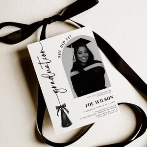 Op de afbeelding: Een afstudeeraankondigingskaart met het woord "graduation" in elegant schrift. De kaart bevat een zwart-witfoto van een afgestudeerde en de tekst "She Did It!" en evenementdetails. Een zwart lint is om de kaart gebonden.