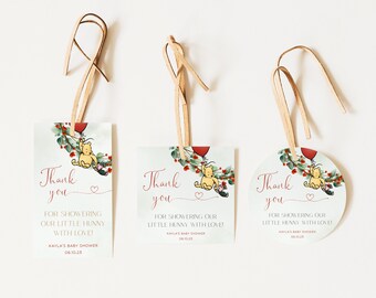 May include: Three Winnie the Pooh themed thank you tags for a baby shower. The tags are printed with a Winnie the Pooh illustration, a red balloon, and greenery. The text on the tags reads "Thank you" and "For showering our little hunny with love!" The tags are attached to twine.