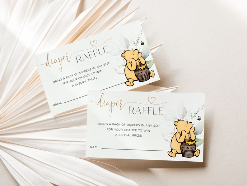 Peut inclure: Deux cartes blanches avec des lettres dor&eacute;es et une illustration de Winnie l'ourson. Le texte sur les cartes indique "tombola couches" et "Apportez un paquet de couches de n'importe quelle taille pour avoir une chance de gagner un prix sp&eacute;cial !"