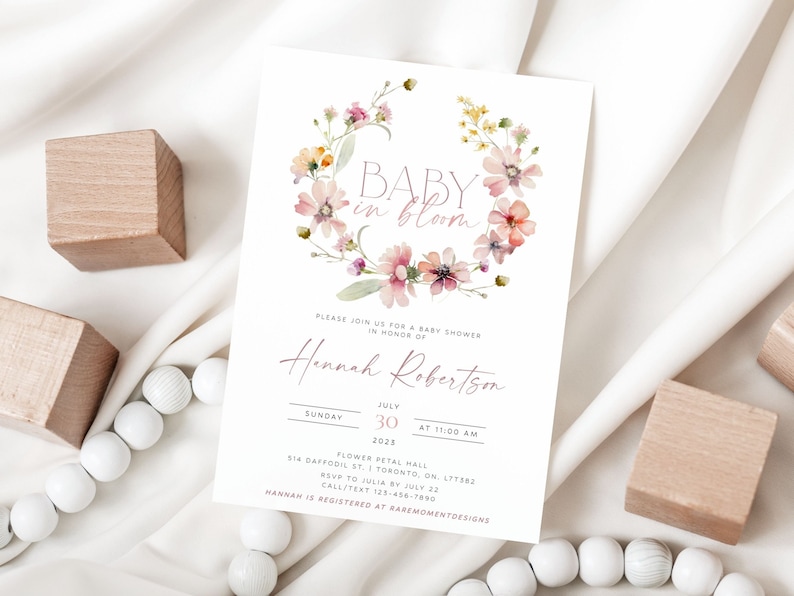 Peut inclure: Une invitation &agrave; une f&ecirc;te pr&eacute;natale avec une couronne florale aquarelle et le texte "BABY in bloom". L'invitation est pour Hannah Robertson et est pr&eacute;vue pour le dimanche 30 juillet 2025 &agrave; 11h00. Le lieu est Flower Petal Hall, 514 Daffodil St., Toronto, ON L1T5B2. RSVP &agrave; Julia avant le 22 juillet, appeler/envoyer un SMS au 123-456-7890. Hannah est inscrite chez RareMomentDesigns.
