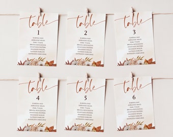 May include: Six wedding table number cards, each with a unique number from one to six. The cards feature a watercolor background and a floral design at the bottom. The word "table" is written in a script font at the top.