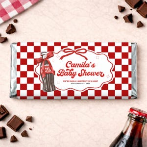 Puede incluir: Envoltorio de barra de chocolate con un patrón de cuadros rojos y blancos. El envoltorio presenta un dibujo de una botella de refresco con un lazo rojo y el texto "Camila's Baby Shower". También se incluye el texto "We're soda lighted you came! September 23, 2020".