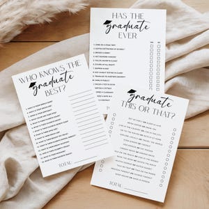 May include: Three white paper game cards with black text for a graduation party. The cards include the phrases "Who Knows the Graduate Best?", "Has the Graduate Ever?", and "Graduate This or That?" on them. The cards are on a beige fabric.