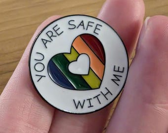 Può includere: Spilla in smalto bianco con un cuore arcobaleno e il testo "You are safe with me".
