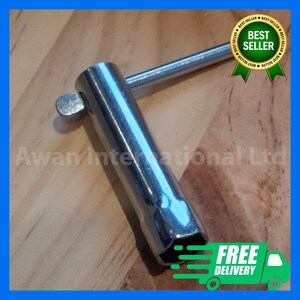 Puede incluir: Una llave de bujías cromada con un encaje hexagonal y un mango. La herramienta está diseñada para uso automotriz y se muestra sobre una superficie de madera. La imagen también incluye el texto "Awan International Ltd" y una insignia de "Best Seller".