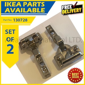 Op de afbeelding: Een set van twee zilverkleurige metalen kastscharnieren met zichtbare montageplaten en stelschroeven. De scharnieren zijn gemarkeerd met Part No: 130728. De tekst IKEA PARTS AVAILABLE en SET OF 2 is weergegeven in blauwe en gele grafische vlakken.
