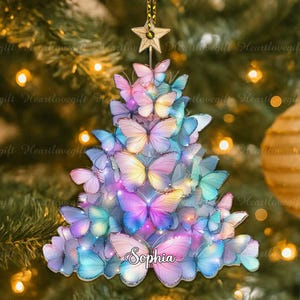 May include: A Christmas tree ornament shaped like a tree, made of colorful butterflies. The butterflies are in shades of pink, blue, purple, and yellow. The name "Sophia" is written on the ornament. A gold star hangs from the top.