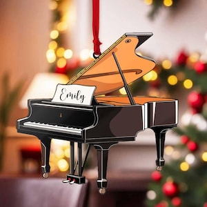 May include: A black and white grand piano Christmas ornament with the name "Emily" written on the music sheet. The piano is decorated with gold accents and has a red ribbon attached to the top.