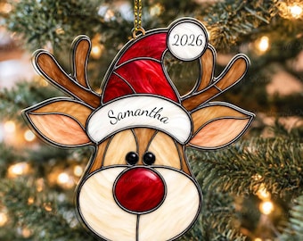 Pode incluir: Um ornamento de rena estilo vitral plano com um gorro vermelho com o texto 2026, uma borda branca com o nome Samantha, chifres castanhos e um nariz vermelho. O ornamento é 2D plano não 3D e pendurado por um fio dourado.