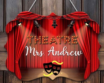 May include: A wooden sign with a red curtain backdrop and spotlights. The sign says "THEATRE Mrs. Andrew" with two theatrical masks in the center.