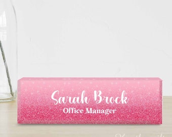May include: Pink glitter desk nameplate with the text "Sarah Brock Office Manager" in white.