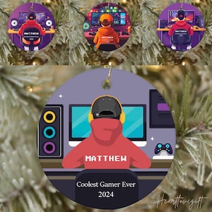 May include: A purple and white round Christmas ornament with a cartoon illustration of a person wearing a red hoodie and headphones, sitting in front of a computer screen. The text "MATTHEW Coolest Gamer Ever 2024" is printed on the ornament.