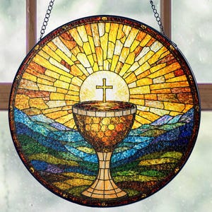 May include: Round stained glass window with a religious theme. The design features a chalice with a cross above it, set against a backdrop of a sunburst and rolling hills. The window is framed in black and hangs from a chain.