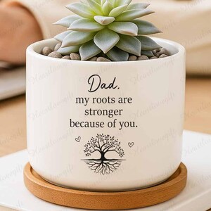 May include: A white ceramic planter with a succulent plant, small stones, and a wooden saucer. The planter has the text "Dad. my roots are stronger because of you." with a tree graphic and hearts.