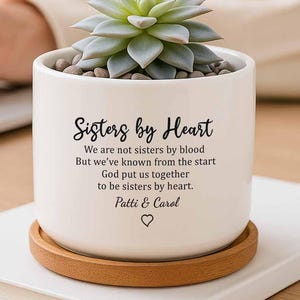 May include: White ceramic planter with a succulent plant inside. The planter has a wood base and a quote that reads "Sisters by Heart. We are not sisters by blood but we've known from the start God put us together to be sisters by heart. Patti & Carol"