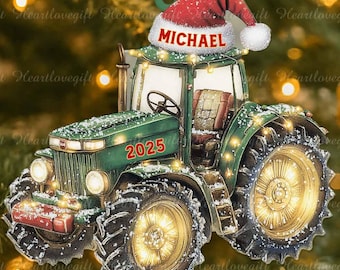 Pode incluir: Um enfeite de Natal de trator verde com o nome "MICHAEL" em um gorro de Papai Noel. O enfeite tem o ano de "2025" na frente e é decorado com luzes. Está pendurado em uma árvore de Natal.