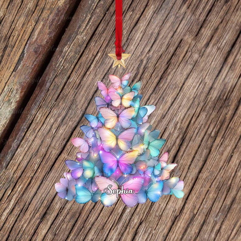 May include: A Christmas tree ornament shaped like a tree, composed of colorful butterflies. The butterflies are in shades of pink, blue, and yellow. A red ribbon and gold star are at the top. The name "Sophia" is written on the bottom.