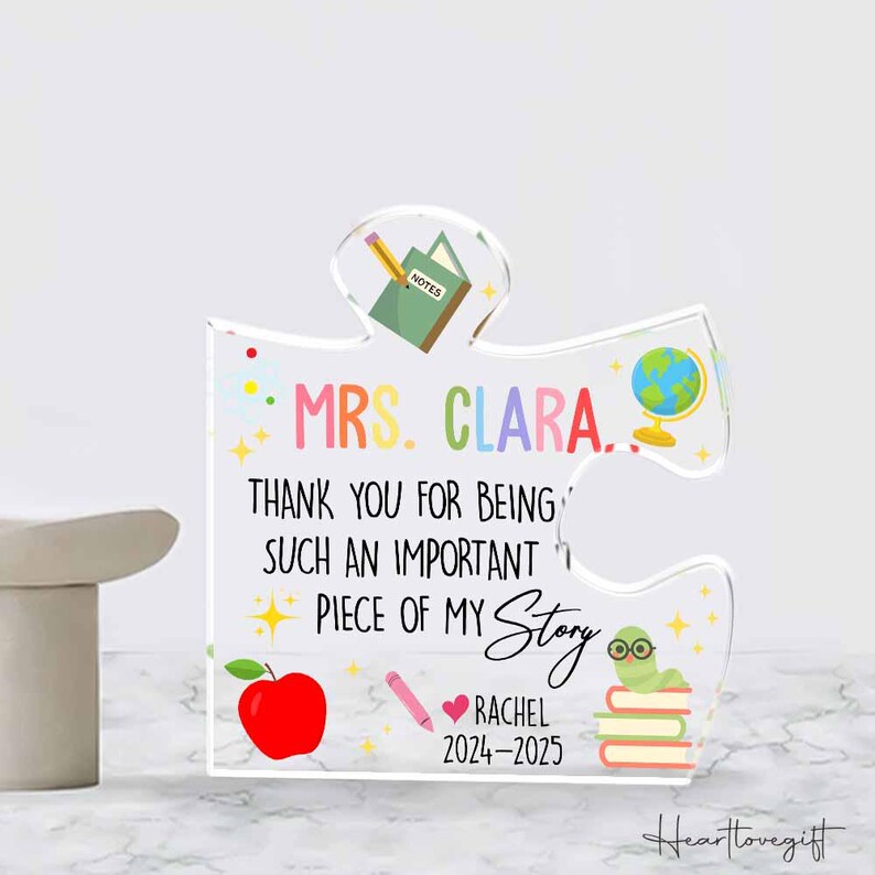 May include: A clear acrylic puzzle piece with colorful illustrations and text. The text reads "MRS. CLARA... THANK YOU FOR BEING SUCH AN IMPORTANT PIECE OF MY Story." Includes a red apple, pencil, globe, and a worm with glasses.