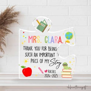 May include: A clear acrylic puzzle piece with colorful text that reads "MRS. CLARA. THANK YOU FOR BEING SUCH AN IMPORTANT PIECE OF MY Story." Includes a red apple, globe, and a worm with glasses.